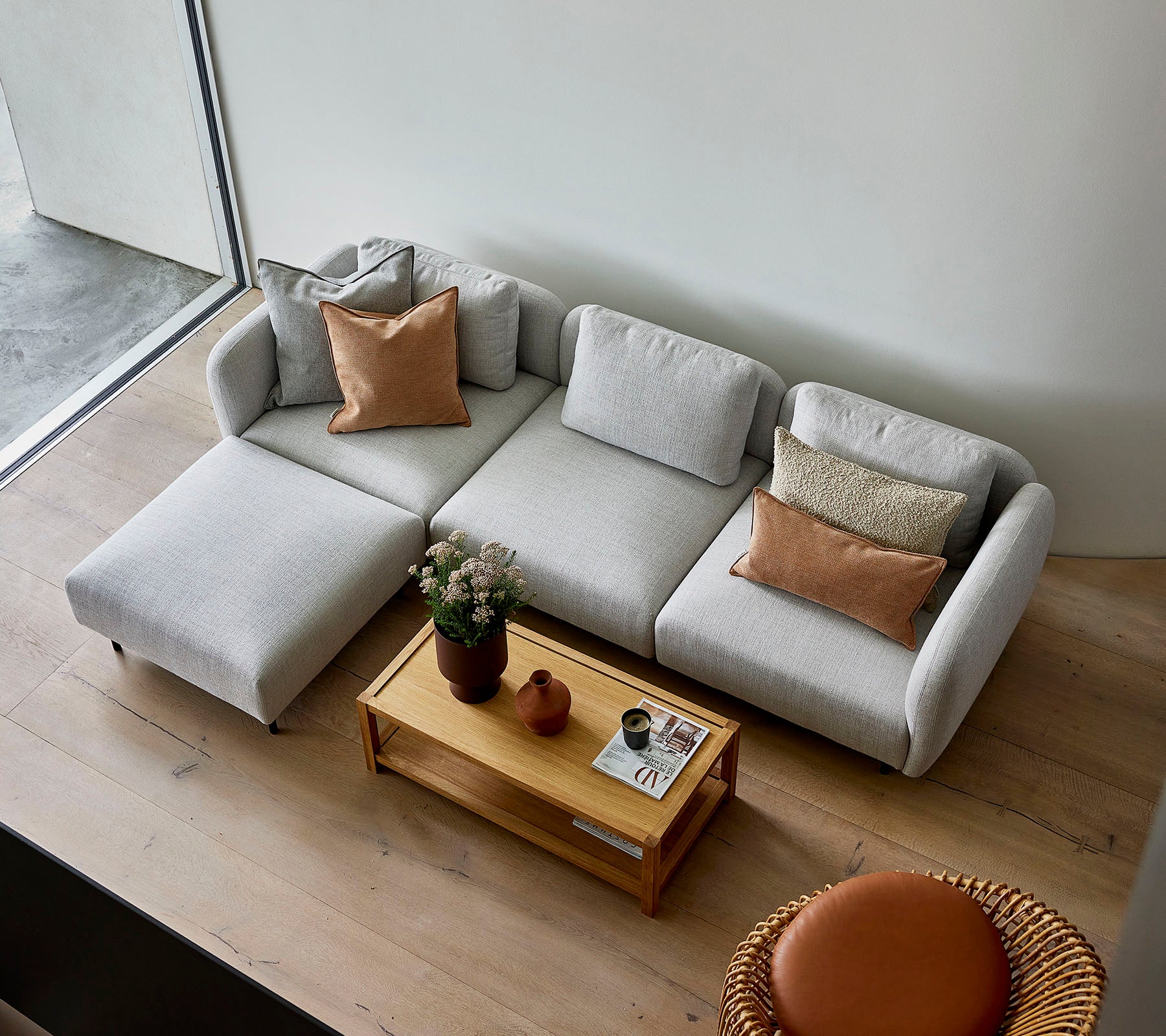 A stylish light gray sectional sofa with pillows, paired with a wooden coffee table and a round seating option, creating a cozy atmosphere.