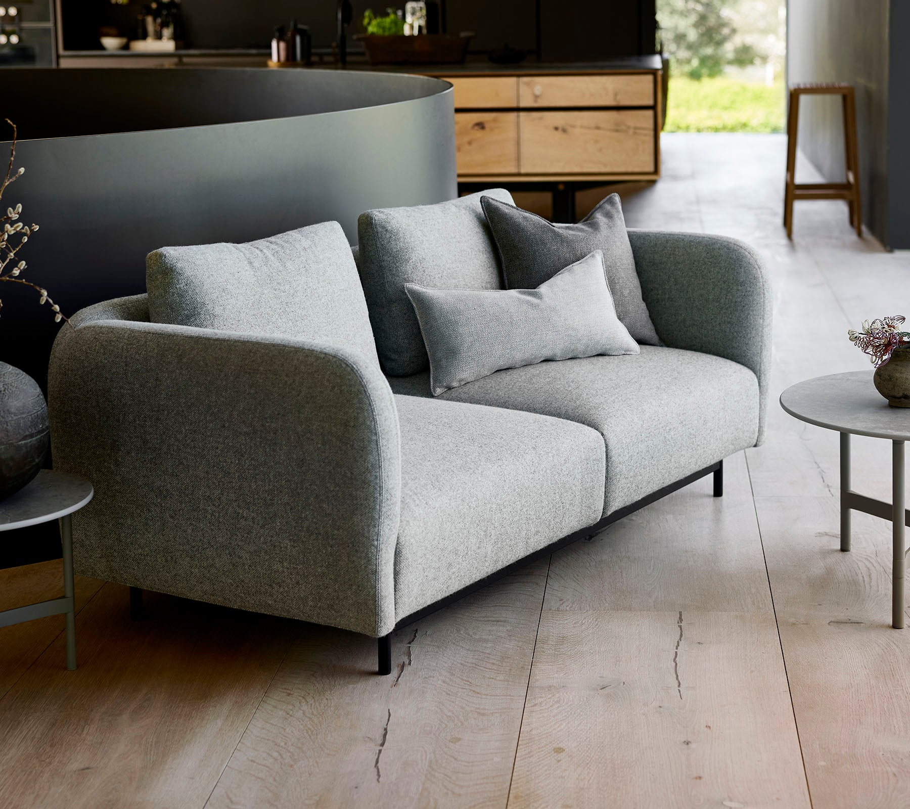 Modern grey sofa with plush cushions, paired with a small round table, set against a minimalist backdrop.