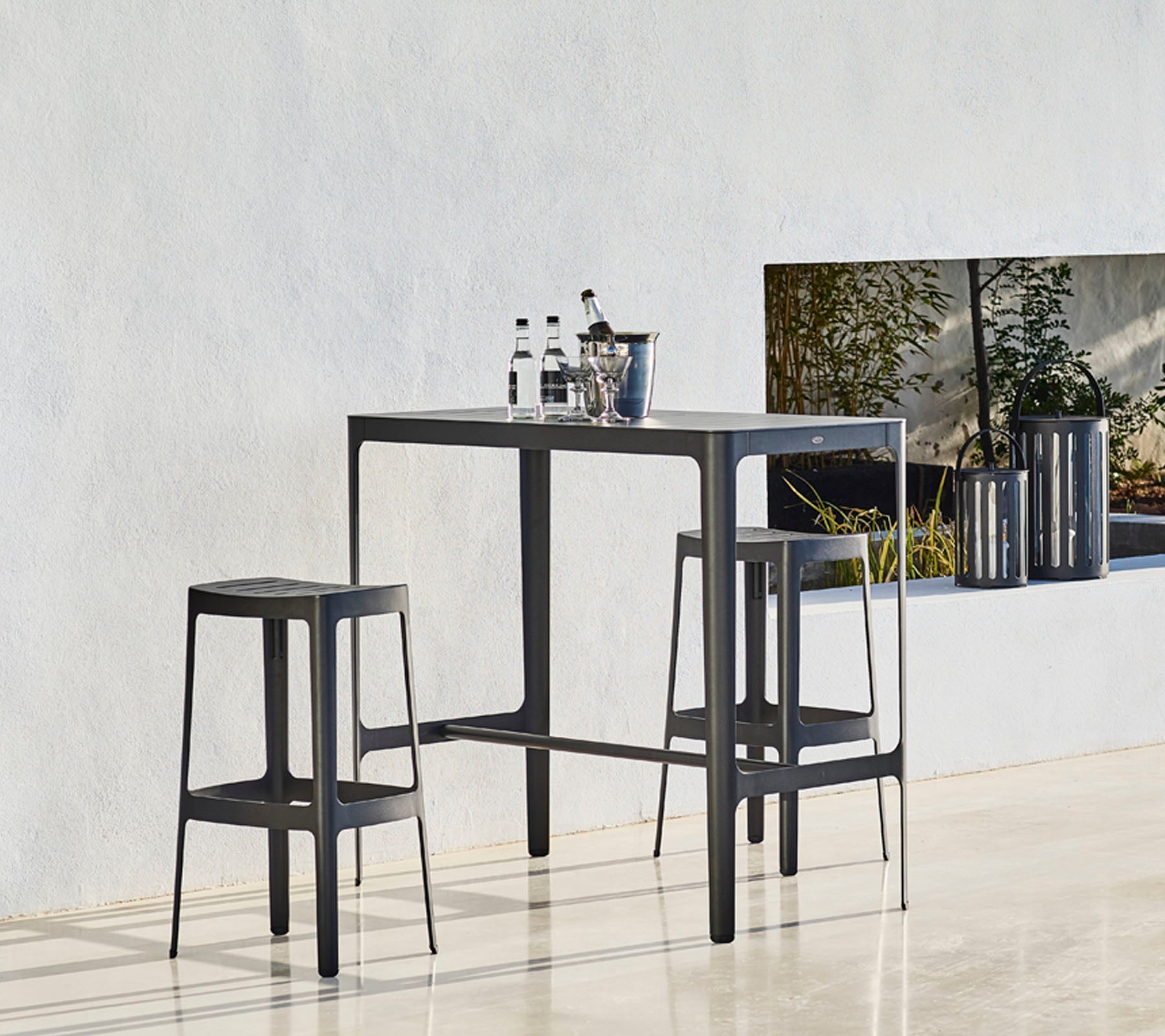 A sleek table set with two matching stools, featuring a minimalist design and bottles placed on top, against a neutral background.
