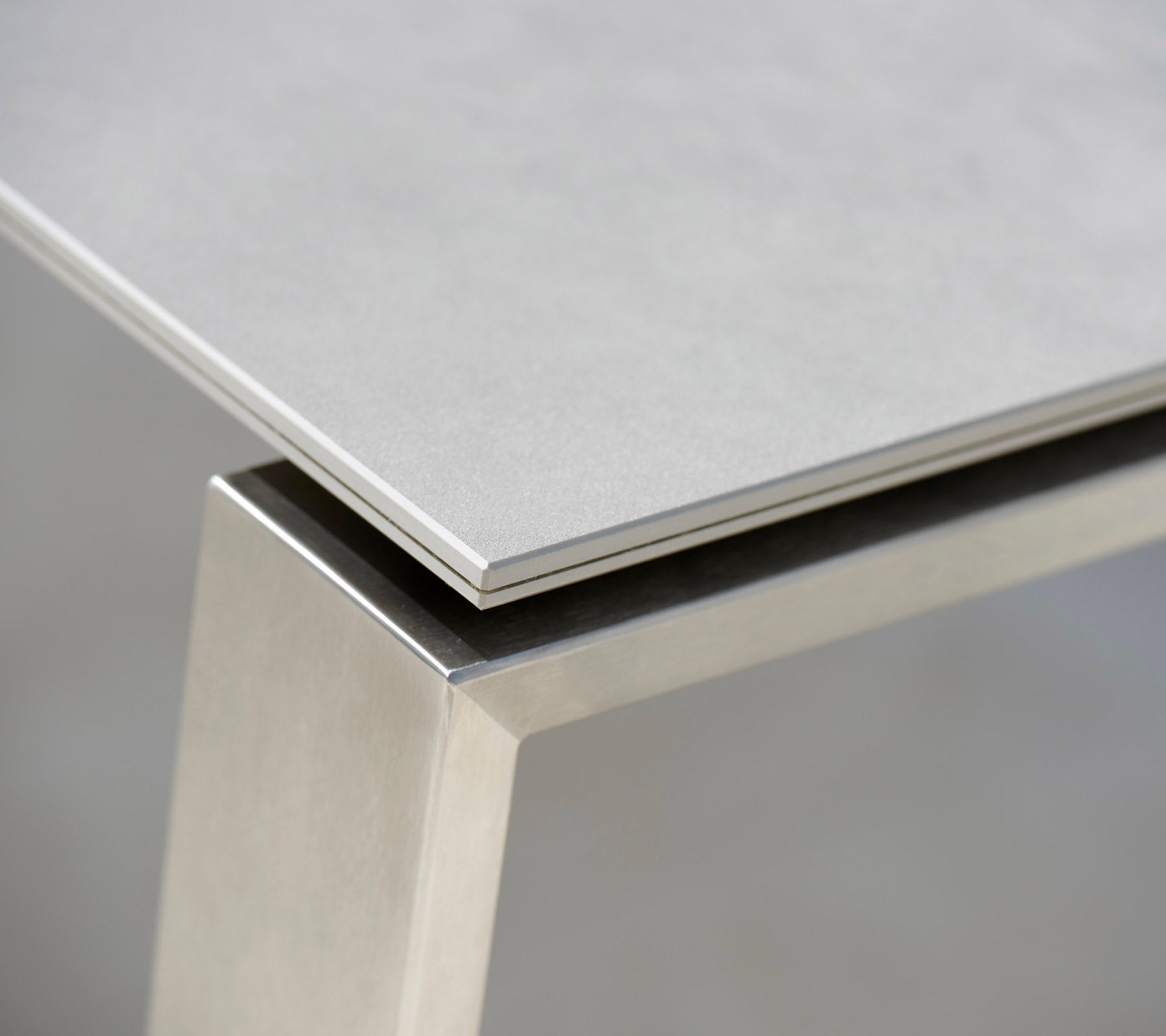 Close-up of a modern table featuring a sleek grey top and a stainless steel base, highlighting the contrasting materials and clean lines.