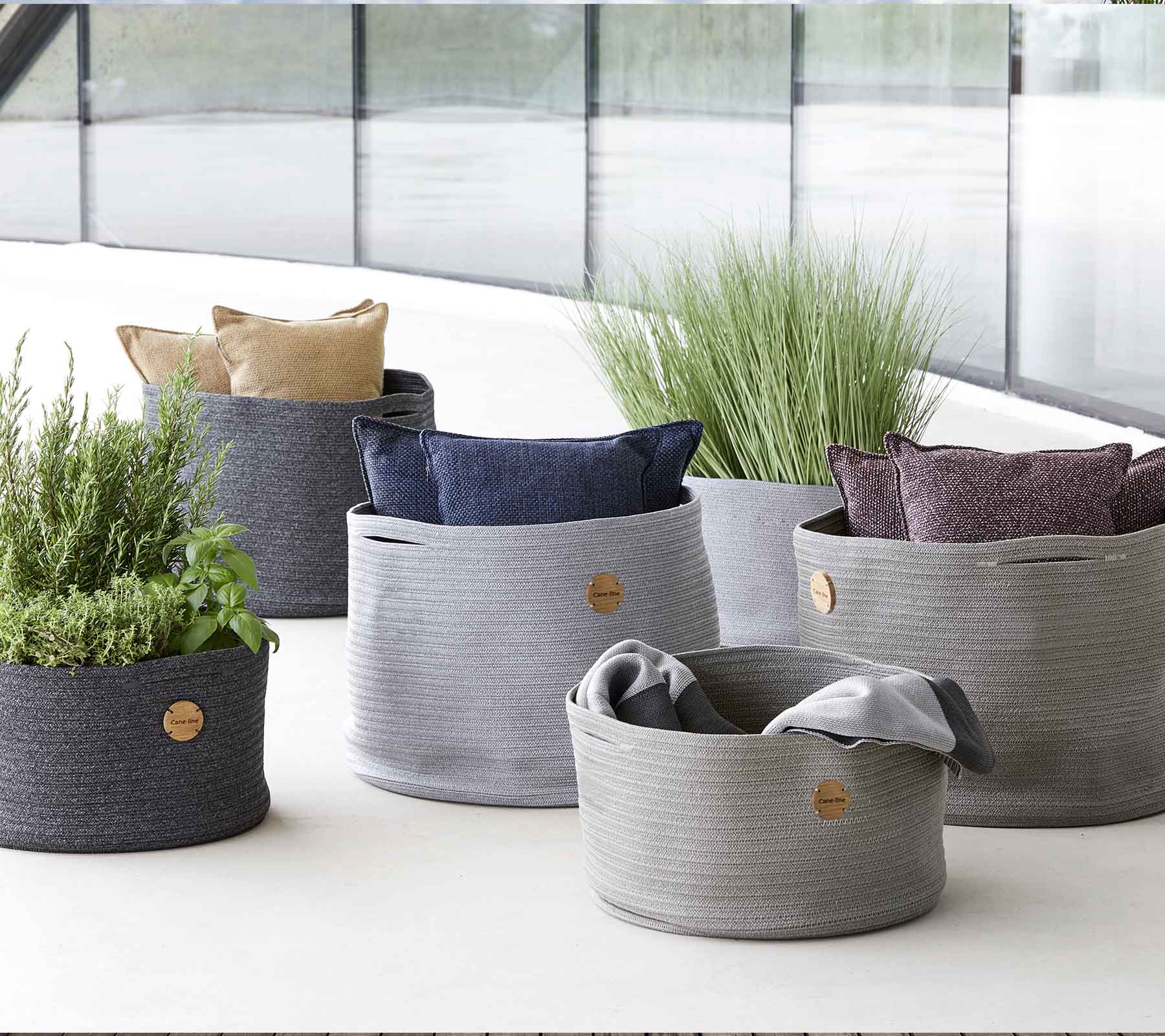 A variety of stylish woven storage baskets in different sizes, featuring vibrant cushions and greenery for a decorative touch.