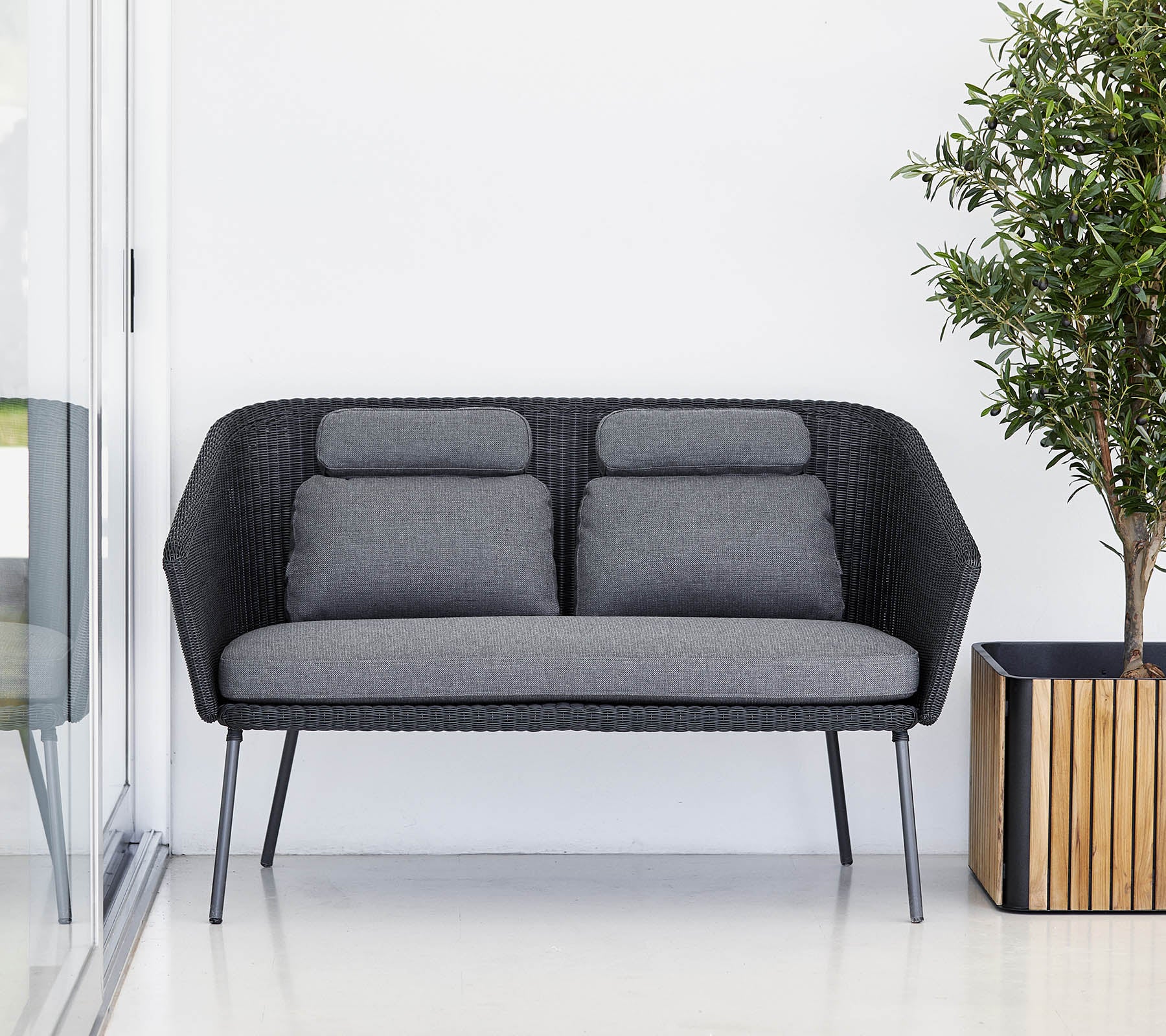 Stylish black sofa with gray cushions, complemented by a potted plant in a wooden planter. Modern and minimalistic design.