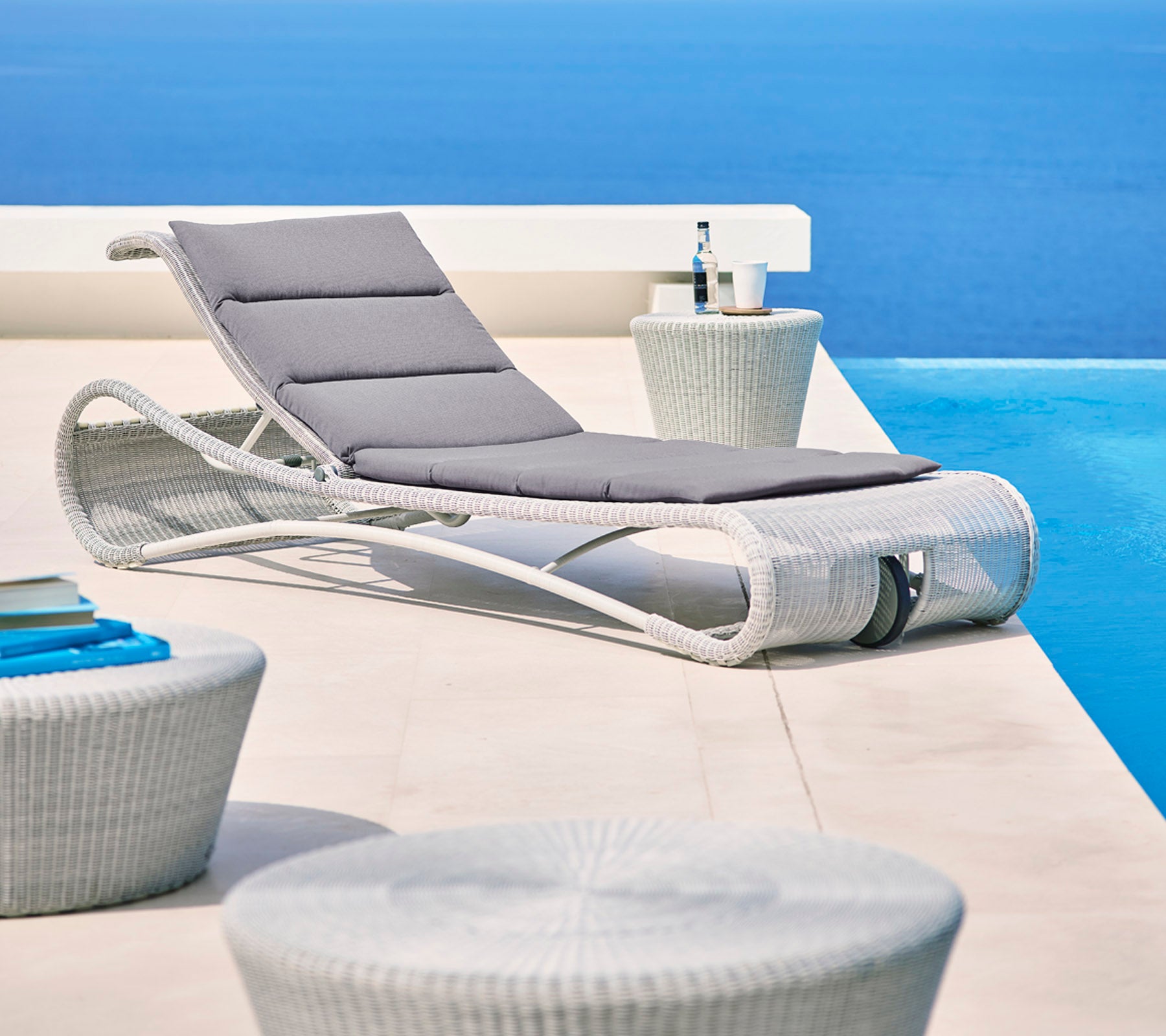 Stylish lounge chair with gray cushion beside modern side tables, set against a serene blue backdrop. Perfect for relaxation.