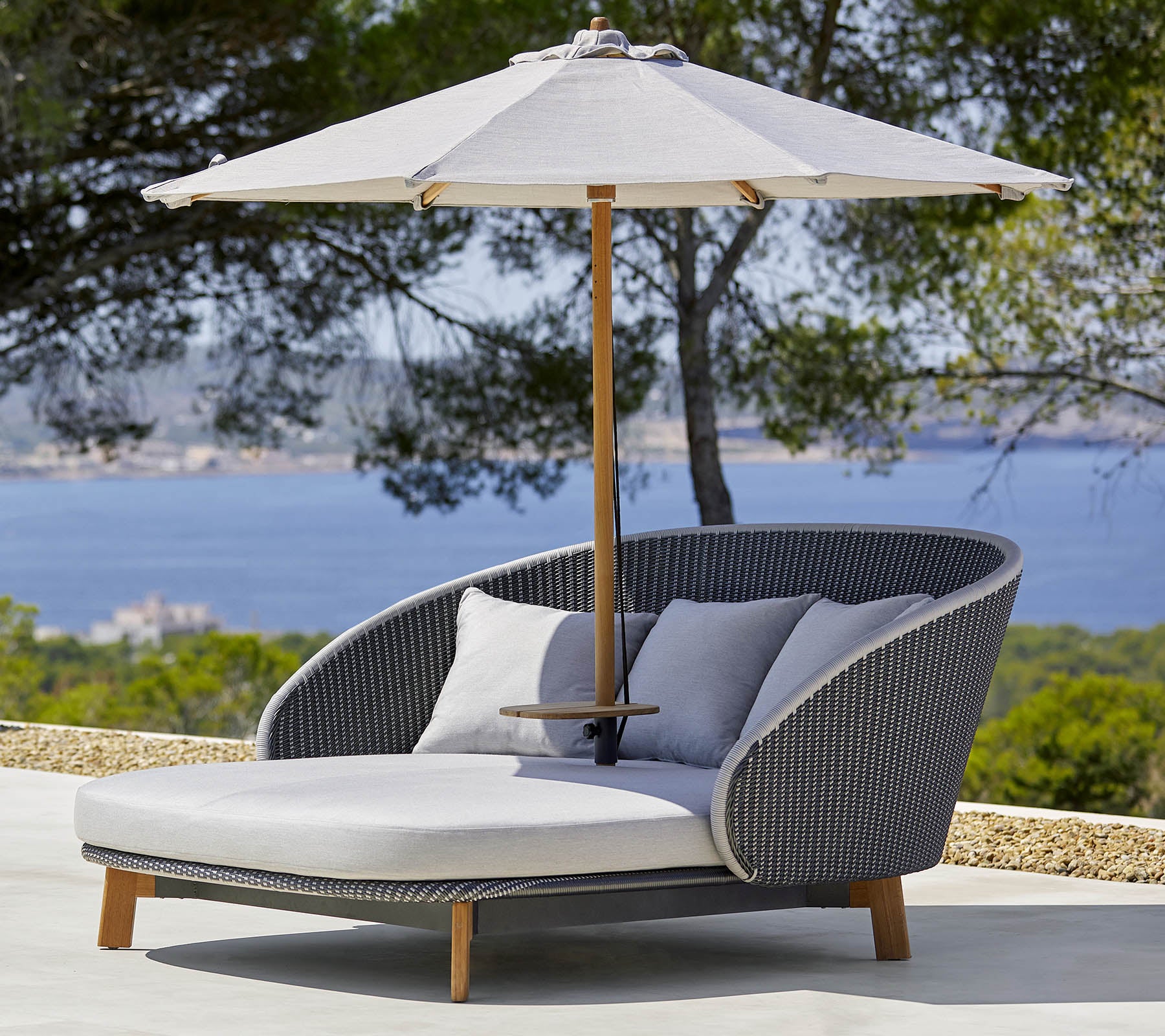 Stylish outdoor lounge chair with comfortable cushions and a large umbrella for shade, set against a scenic backdrop.
