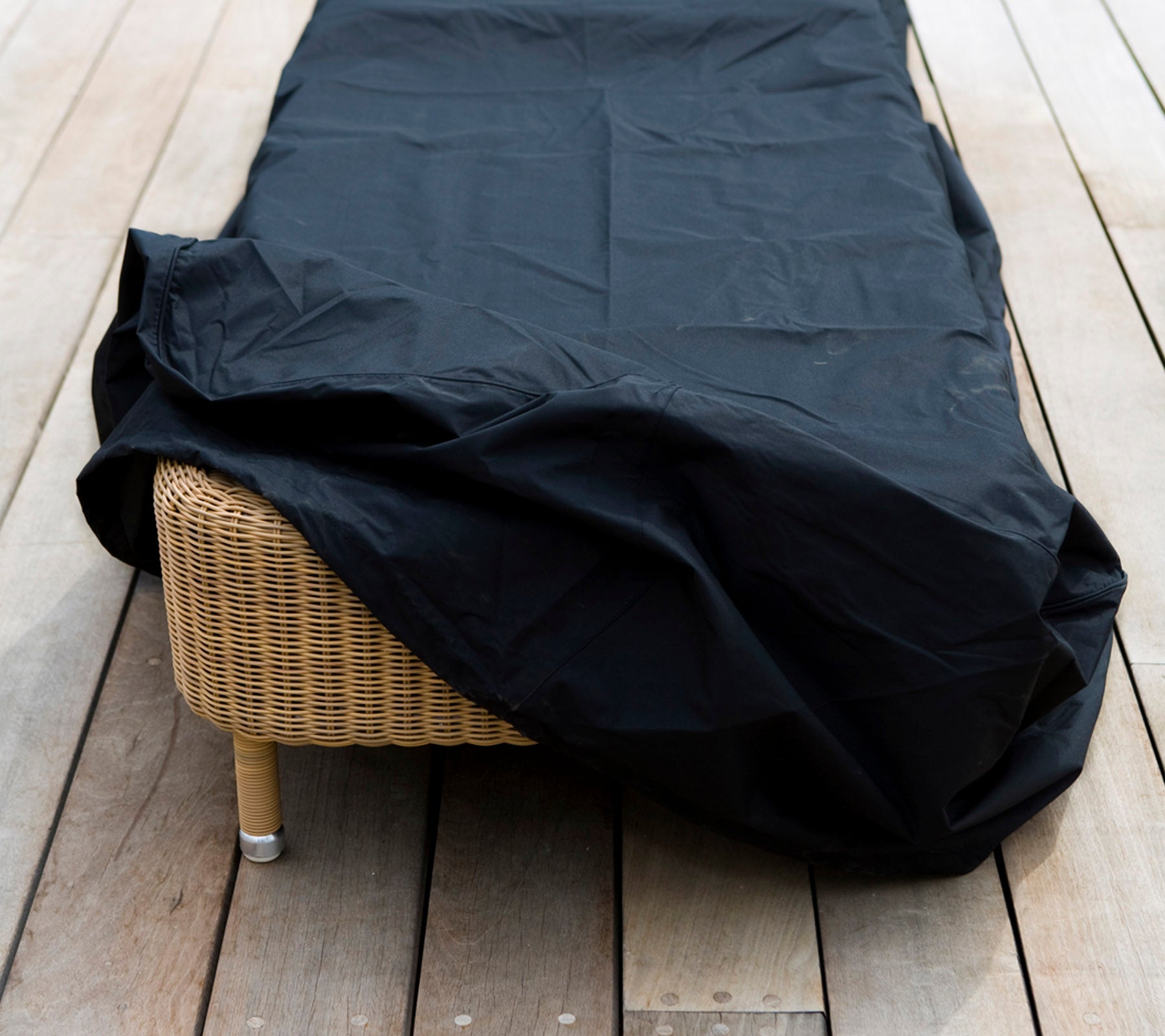A wicker furniture piece covered with a black protective cover, placed on a wooden surface.
