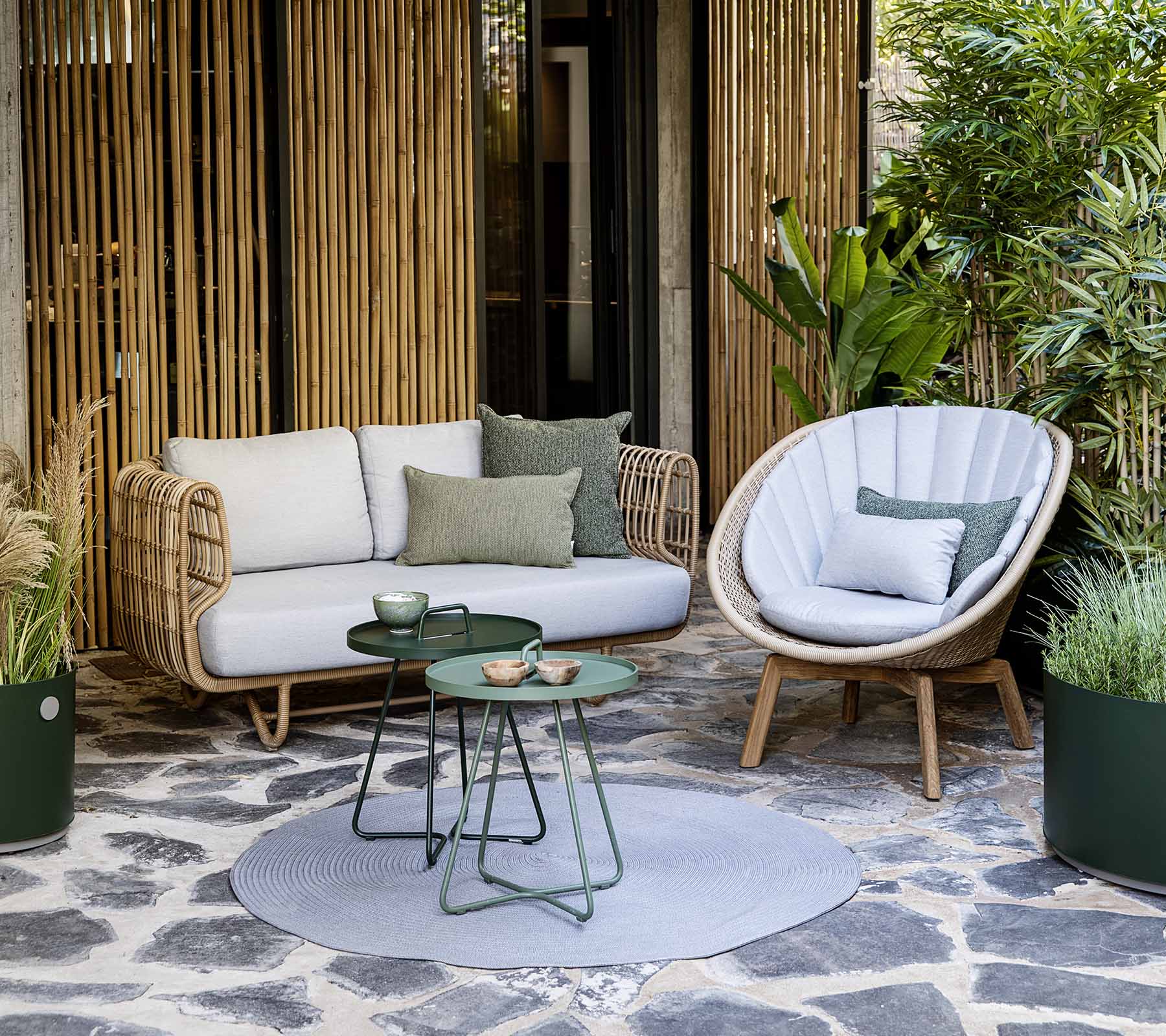 A cozy seating arrangement featuring a rattan sofa and a stylish chair, accompanied by a small table and decorative plants.