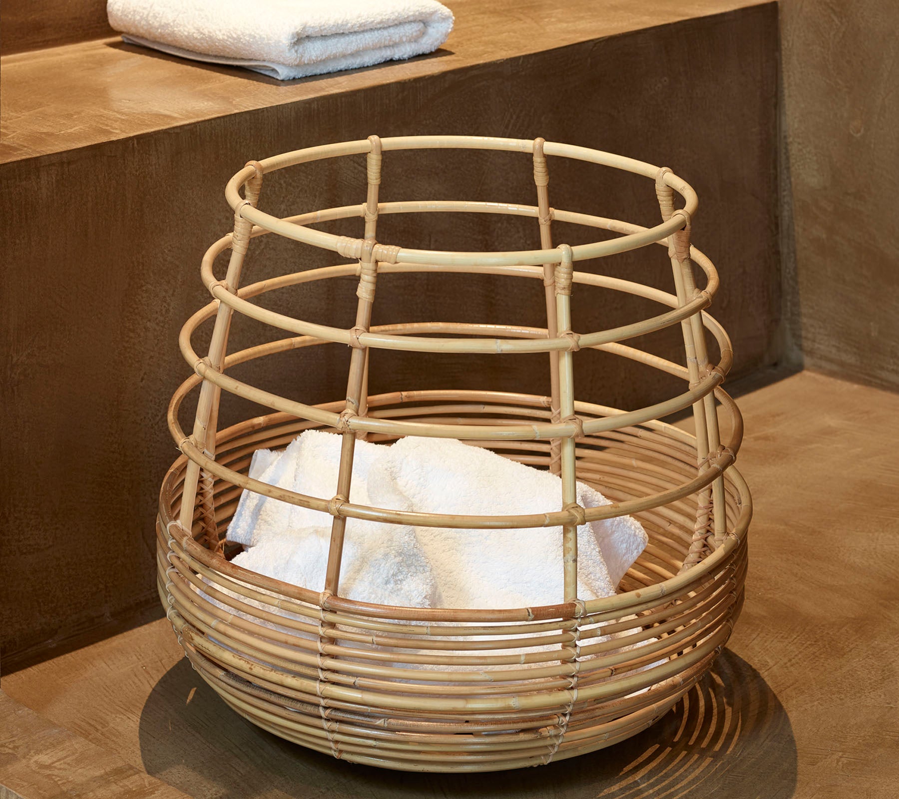 Woven bamboo basket containing neatly stacked white towels, placed on a smooth surface.