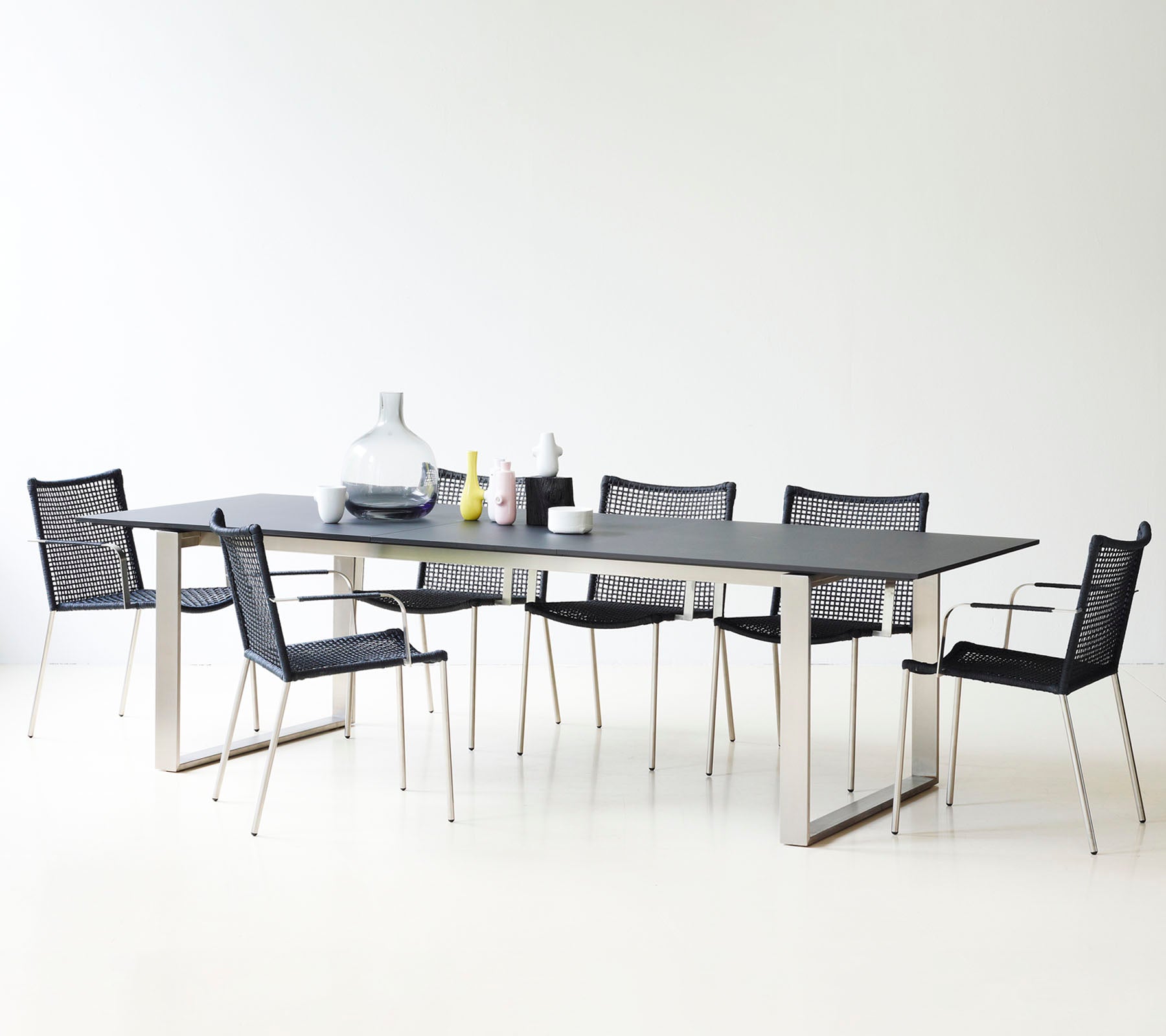 A modern dining table with a sleek design, surrounded by stylish black mesh chairs and decorative vases.