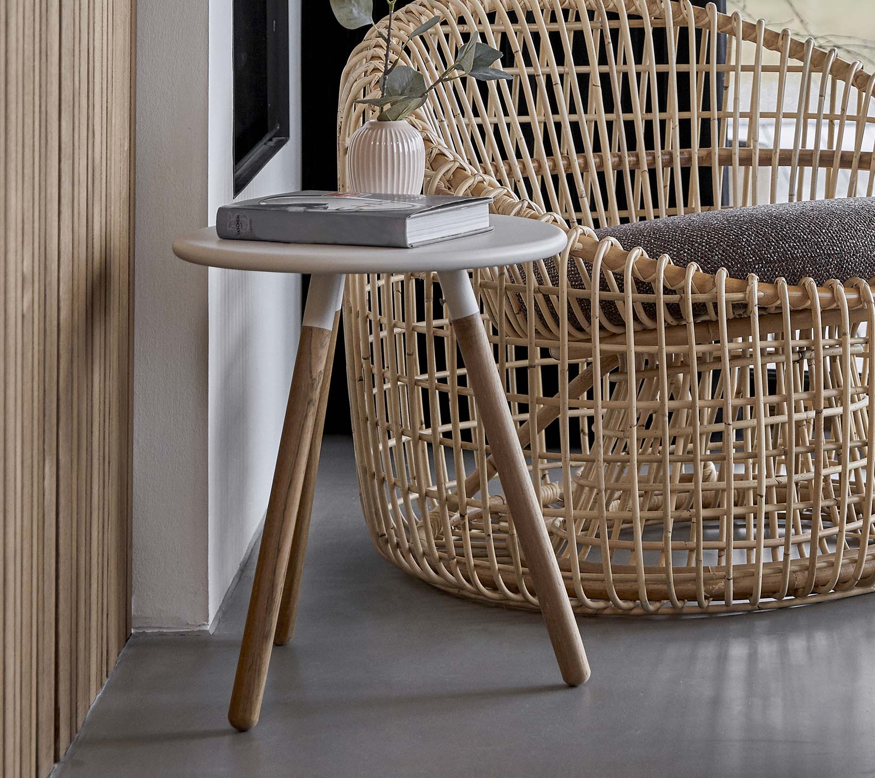 A round side table with a light-colored surface and wooden legs, positioned next to a woven chair.