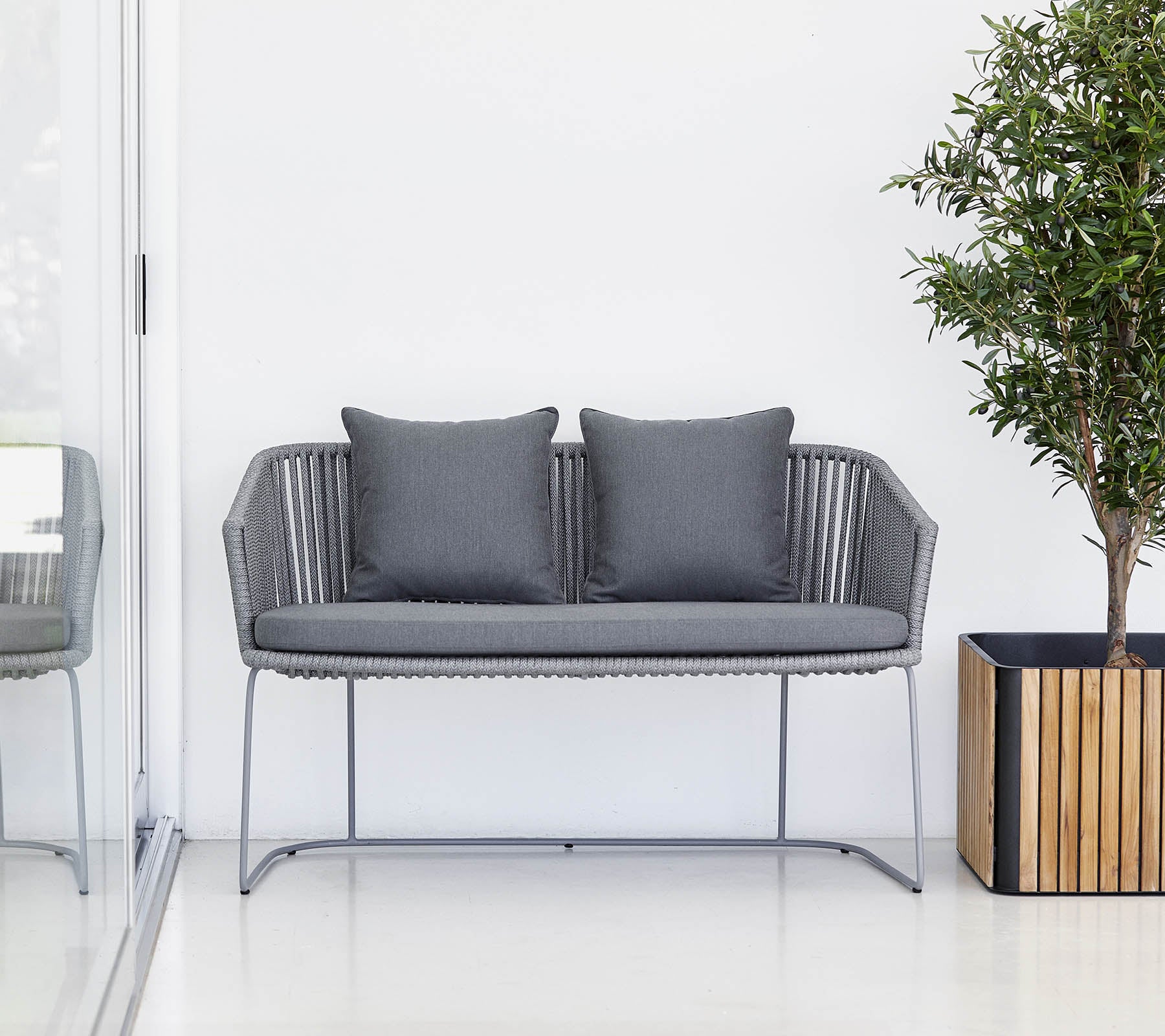 A modern gray two-seat sofa with cushions, accompanied by a potted plant and a wooden planter.