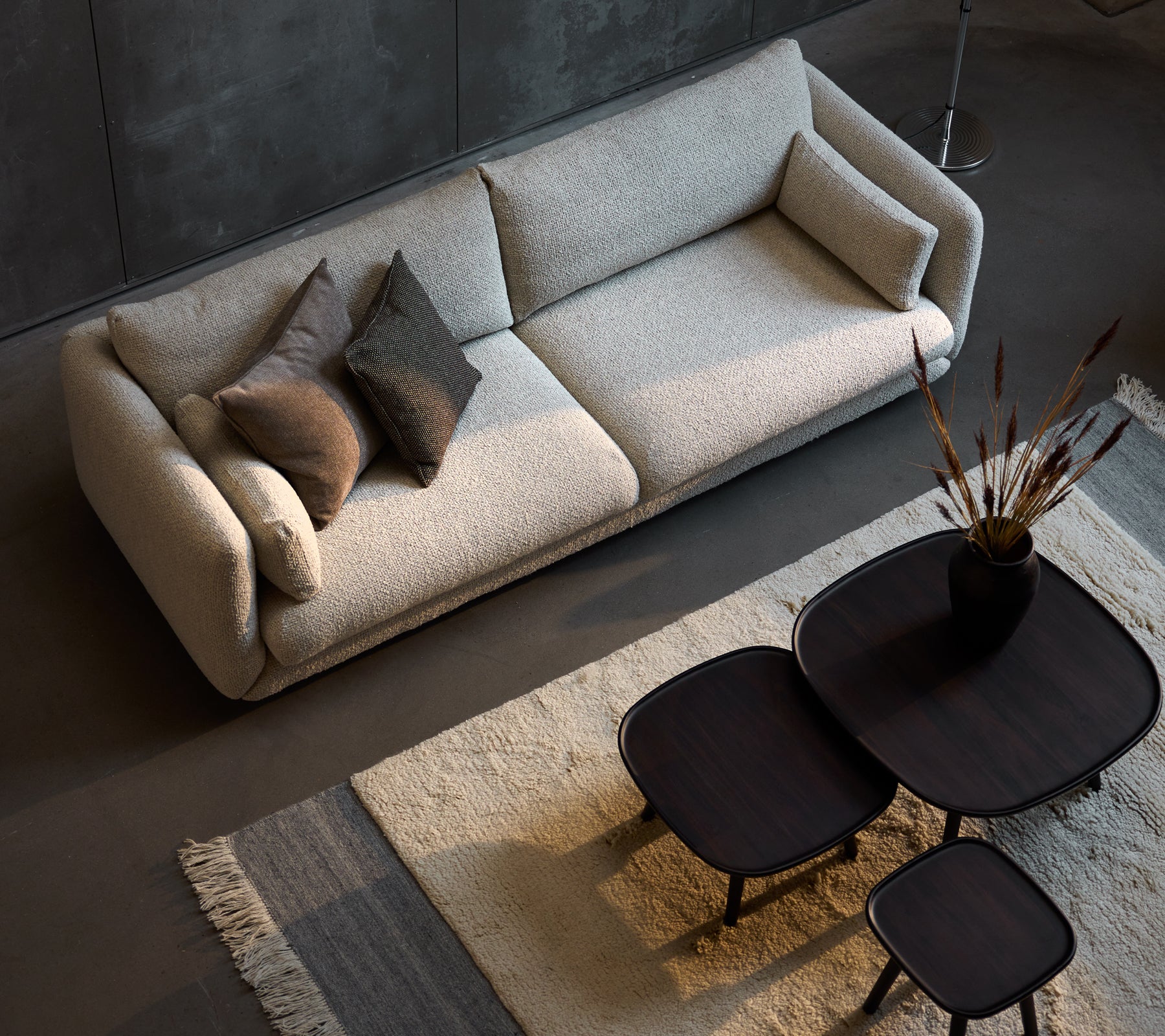 Stylish three-seater sofa in sand flair, complemented by three sizes of sleek black coffee tables and decorative pillows.