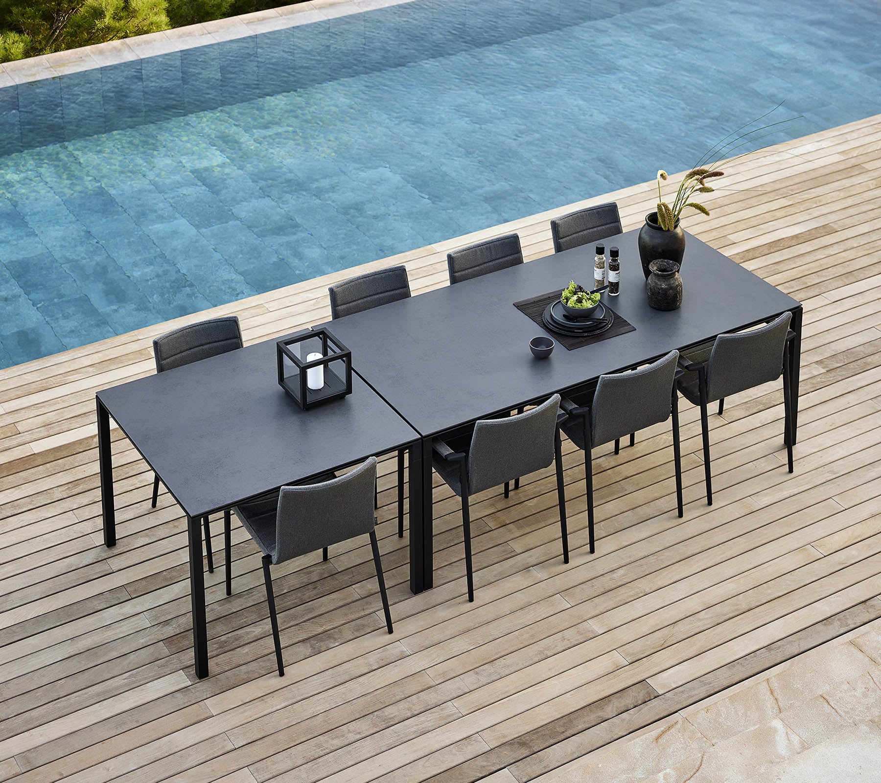A sleek dining setup featuring a pure table with modern chairs, adorned with decorative plants and accessories, beside a tranquil pool.