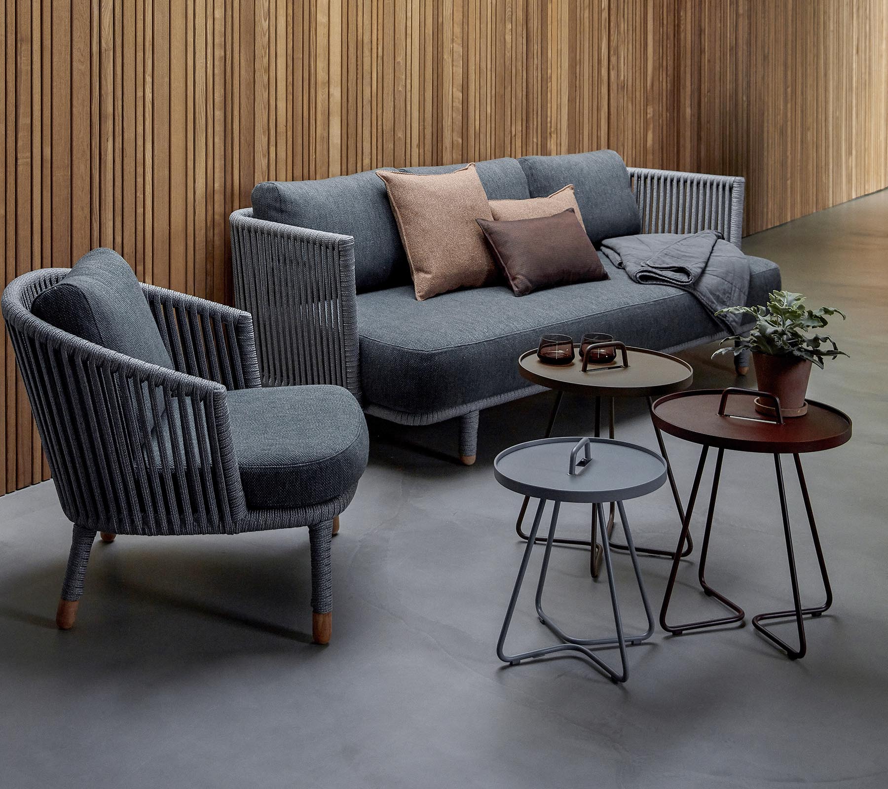 Stylish seating arrangement featuring a grey sofa with cushions and two accent chairs, accompanied by three modern tables and a potted plant.