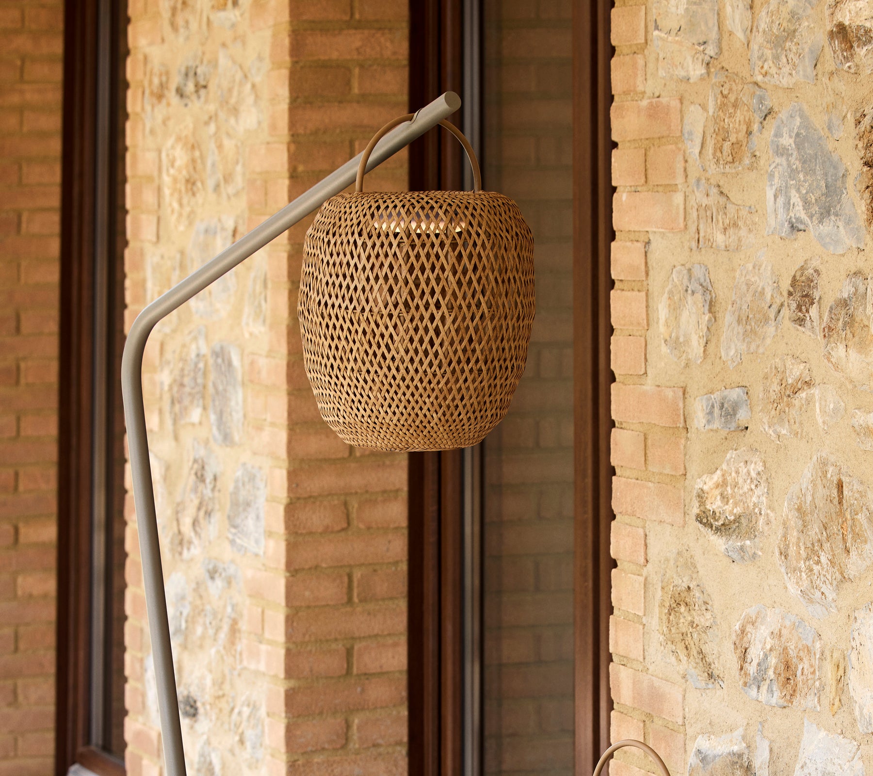 A woven glowing lamp suspended from a sleek stand, complementing a textured stone wall.