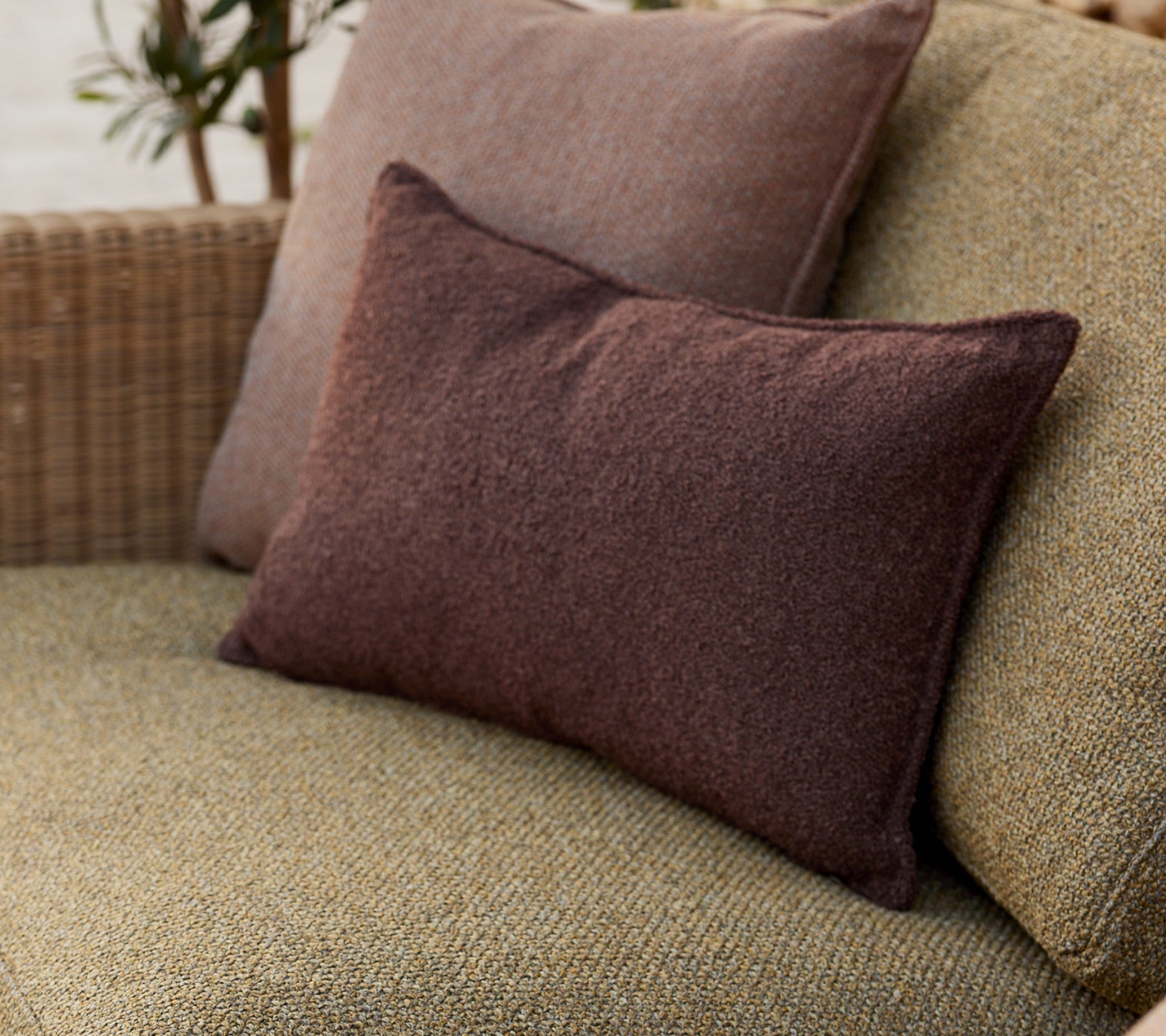 Soft decorative cushions in earthy tones, arranged comfortably on a woven surface, adding a cozy touch to the setting.