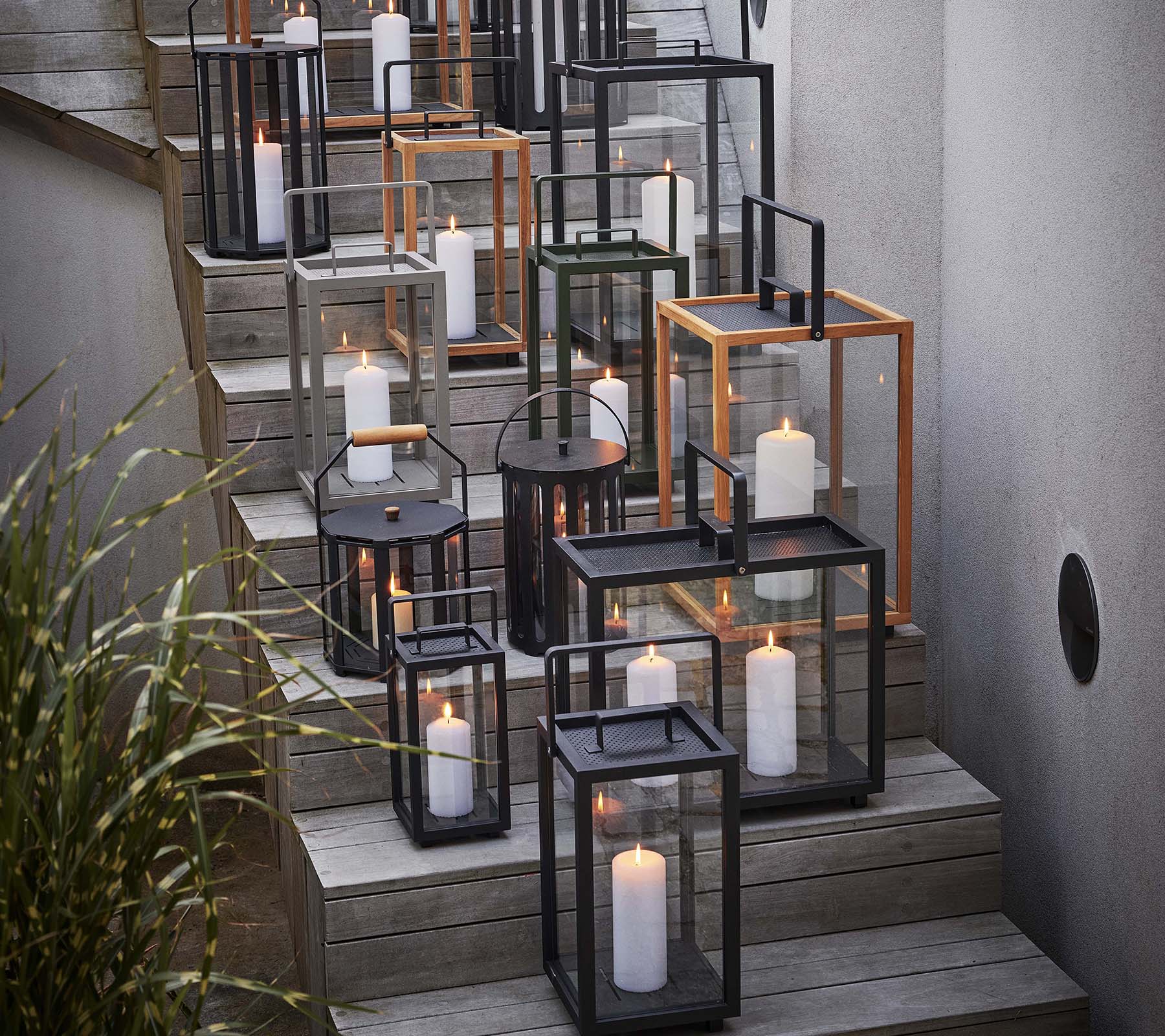 A collection of various lanterns with candles arranged on a staircase, showcasing a mix of black and metallic frames.