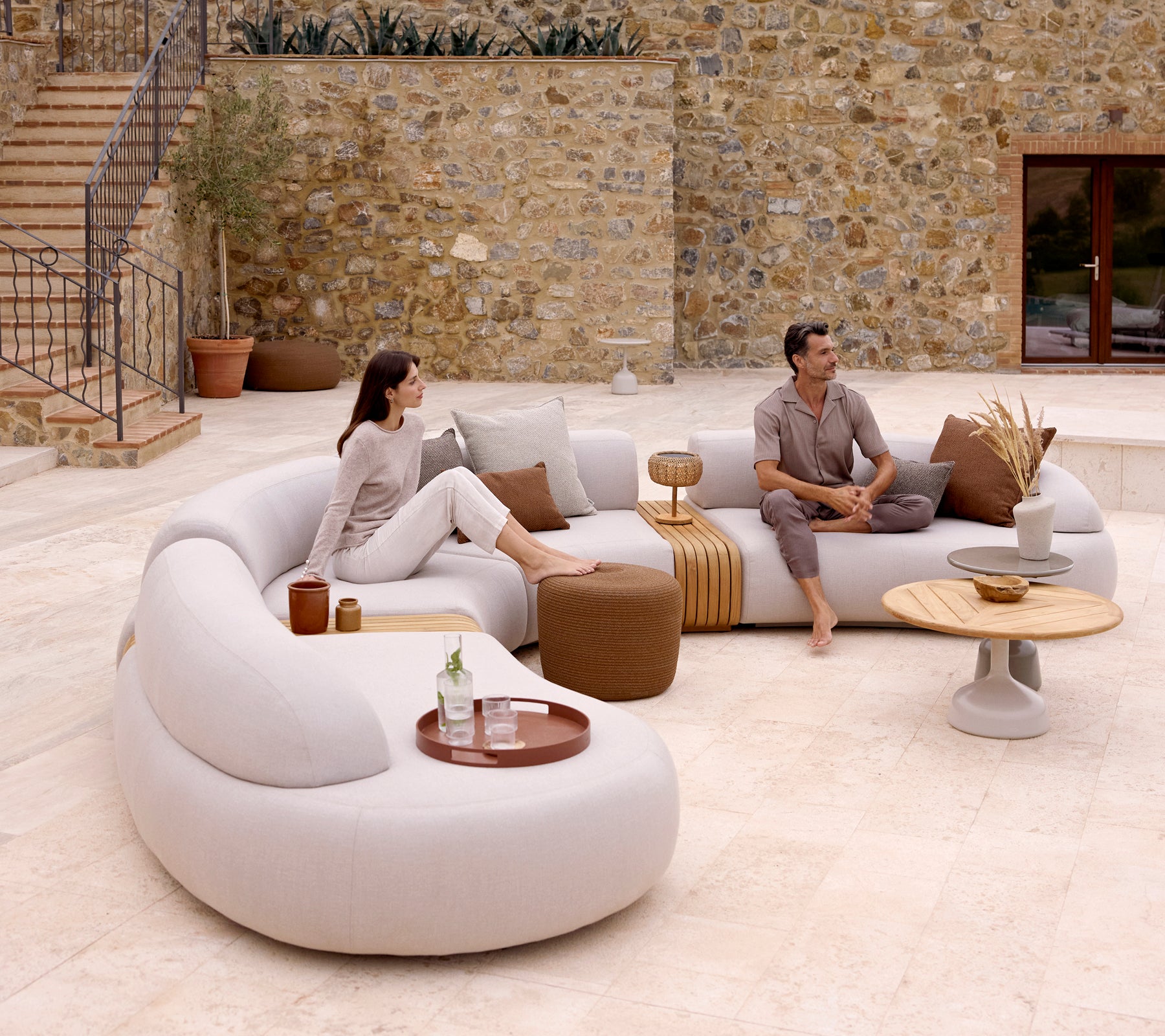 A modern lounge setup featuring a curved sofa, a circle footstool, and a stylish coffee table with a club tray, creating a cozy ambiance.