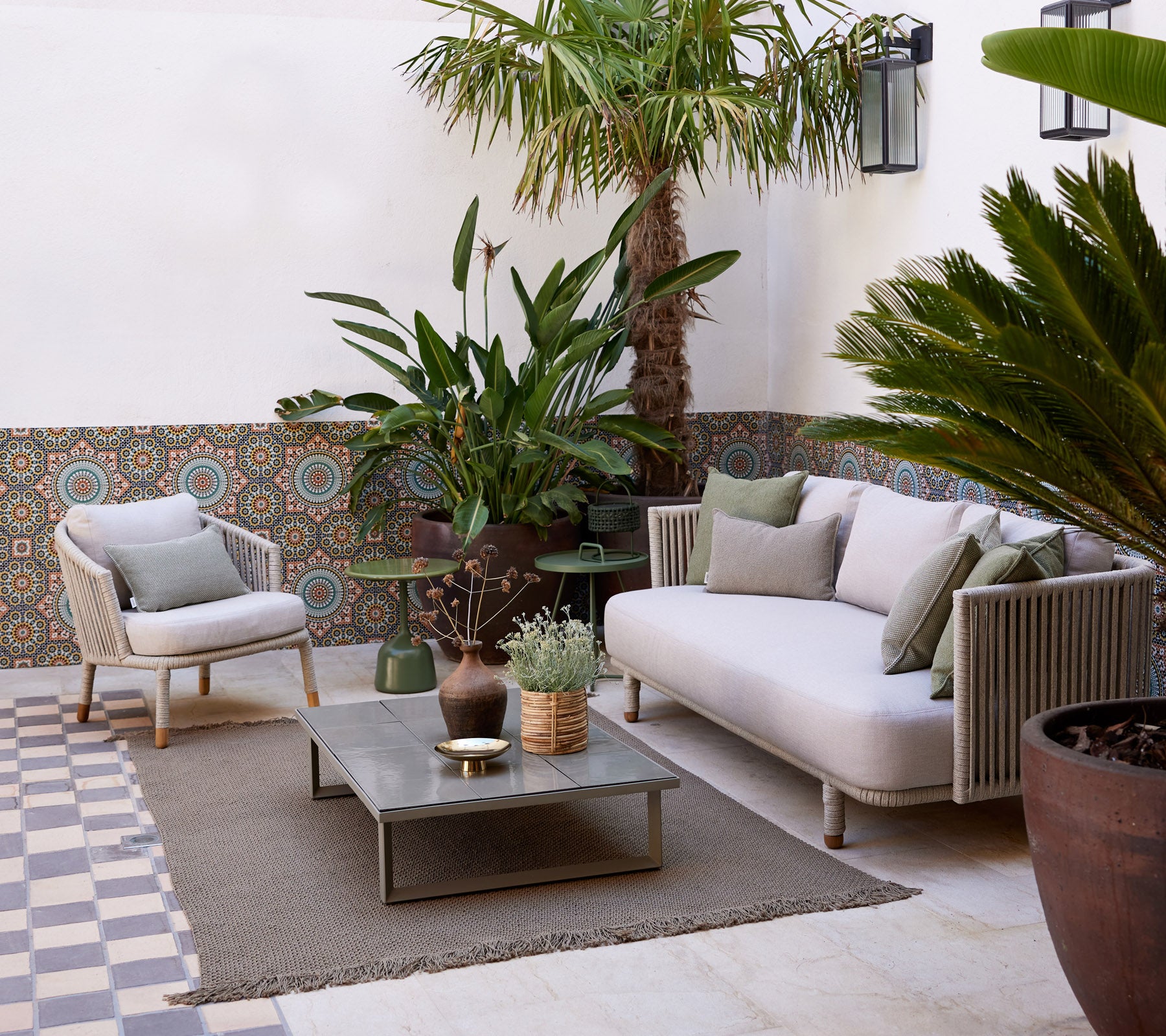 Cozy lounge area featuring a light sofa, potted plants, decorative table, and textured flooring, creating a serene ambiance.