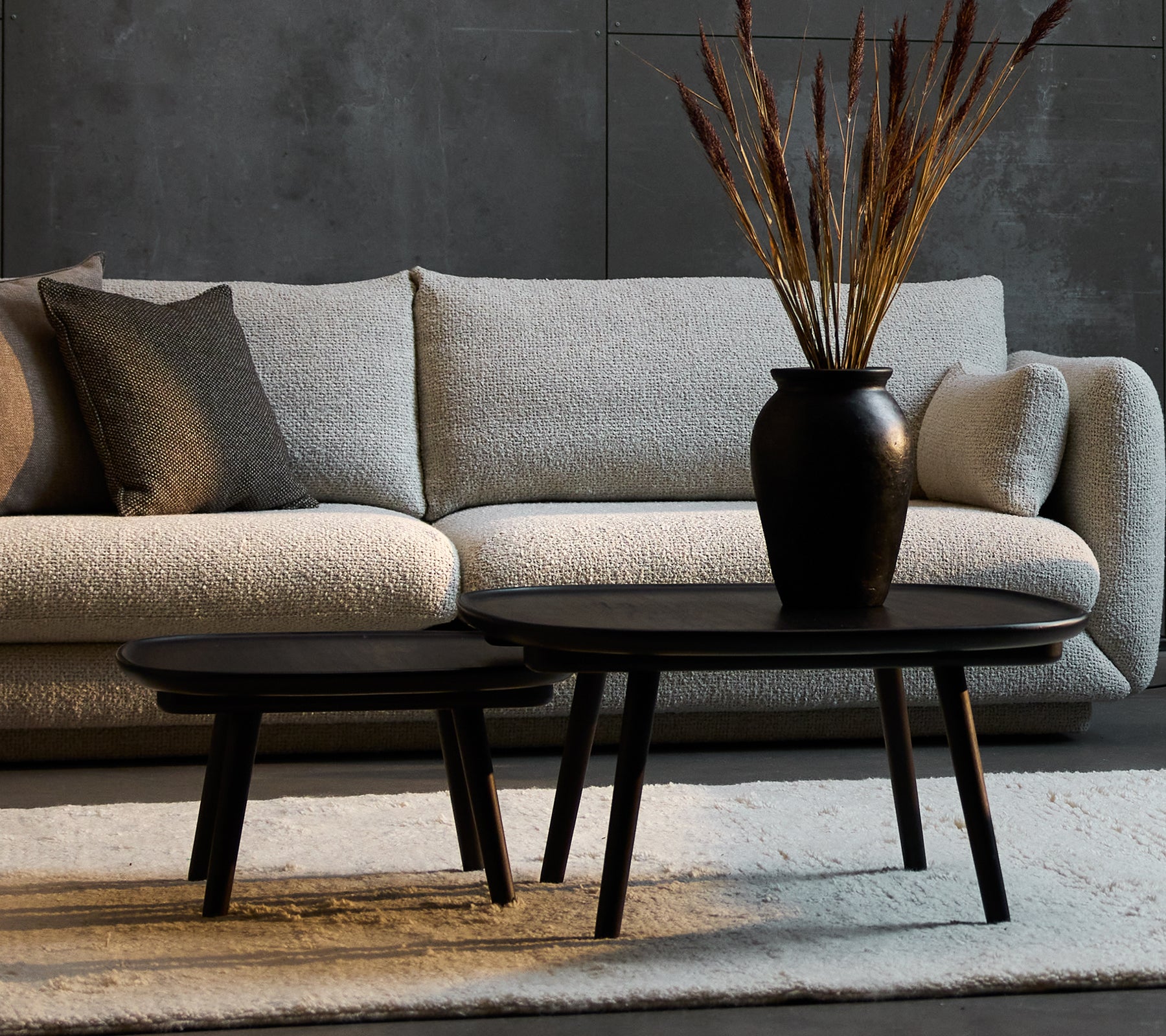 Two elegant black coffee tables in varying sizes, complemented by a decorative vase with dried plants, set against a cozy sofa.