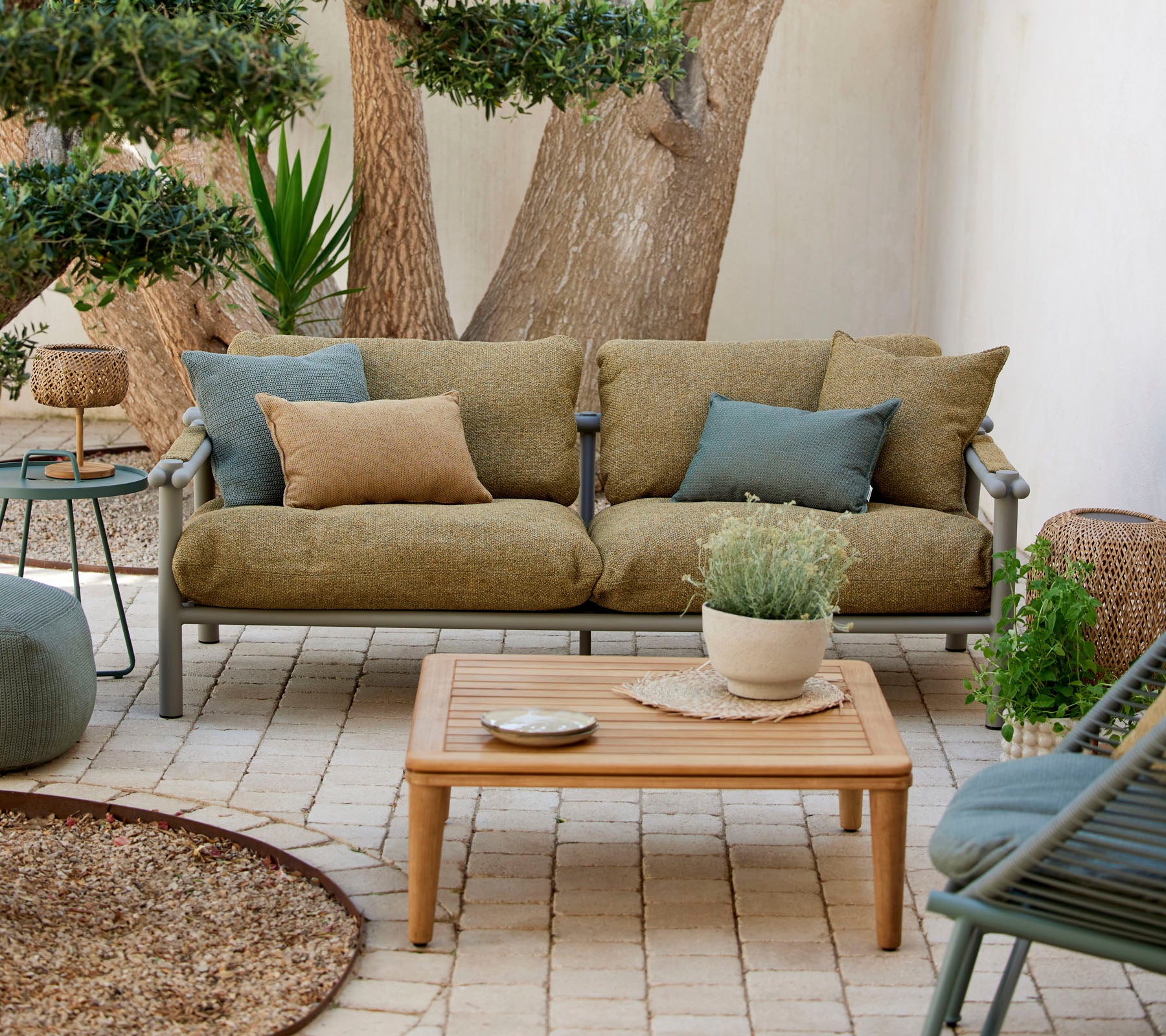 Comfortable seating area featuring a green sofa with cushions, a wooden coffee table, and decorative plants in a serene setting.